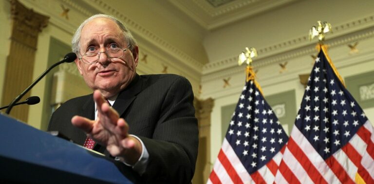 Senator Levin giving a speech flanked by U.S. flags