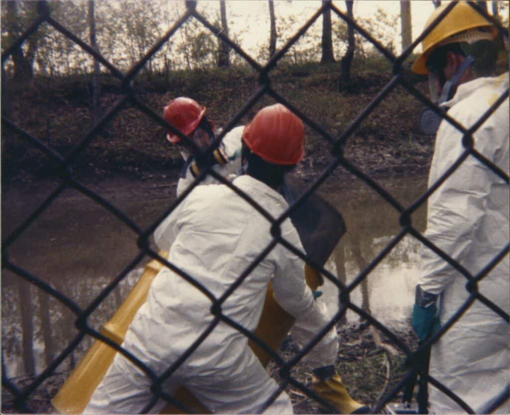 Workers behind a fence in caps and protective suits